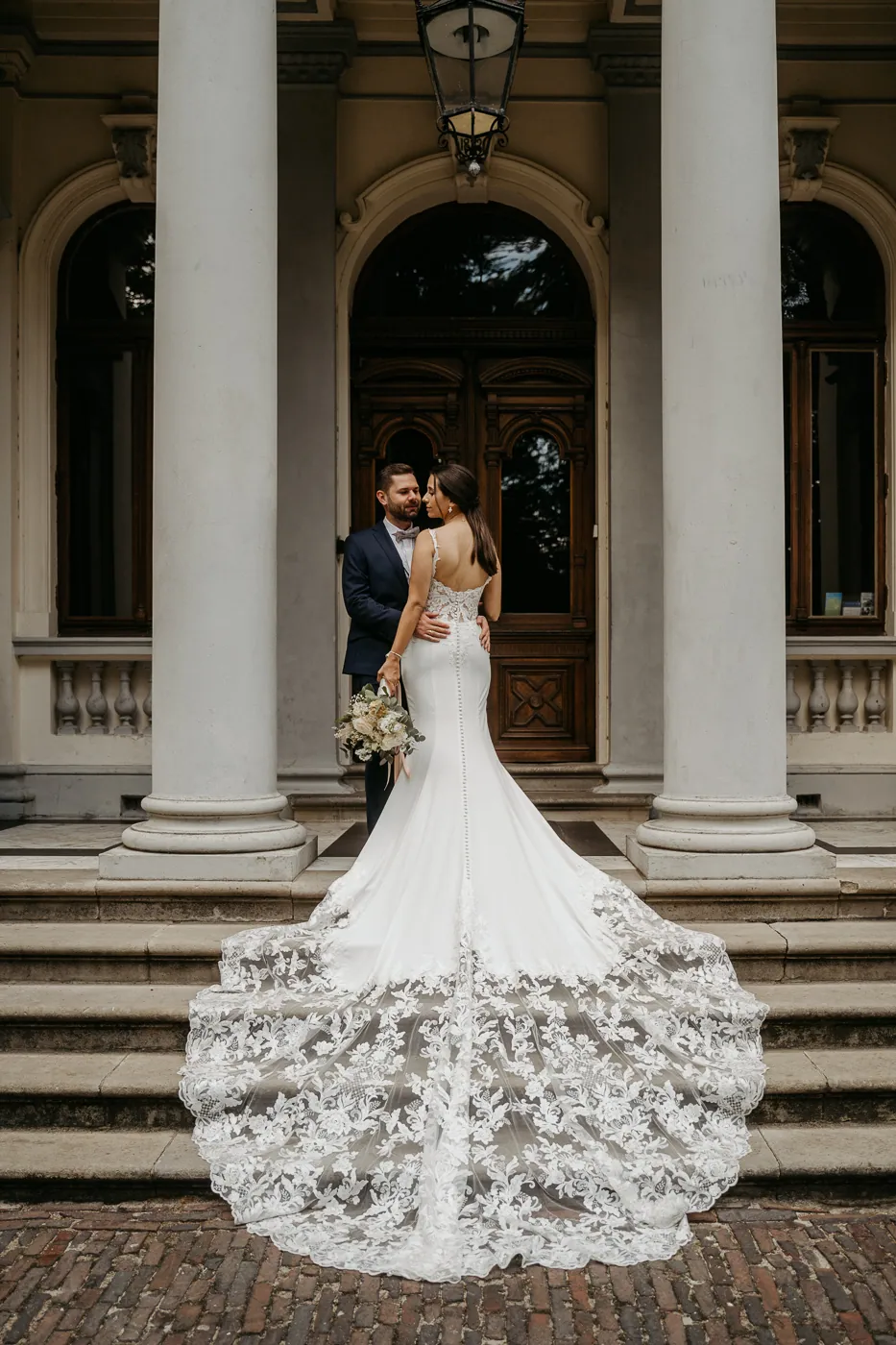 Jenny und Chris gehen Hand in Hand die Stufen einer Villa mit Säulen hinunter