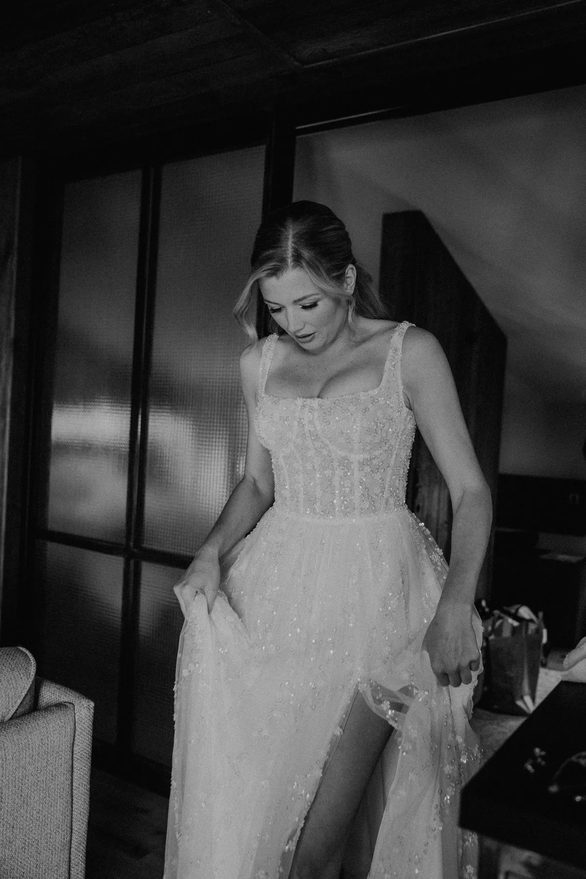 Schwarzweißaufnahme: Neele rafft im paillettenbestickten Brautkleid mit Corsage den Rock und blickt an sich herab, durch den Beinschlitz zeigt sich ihr Bein.