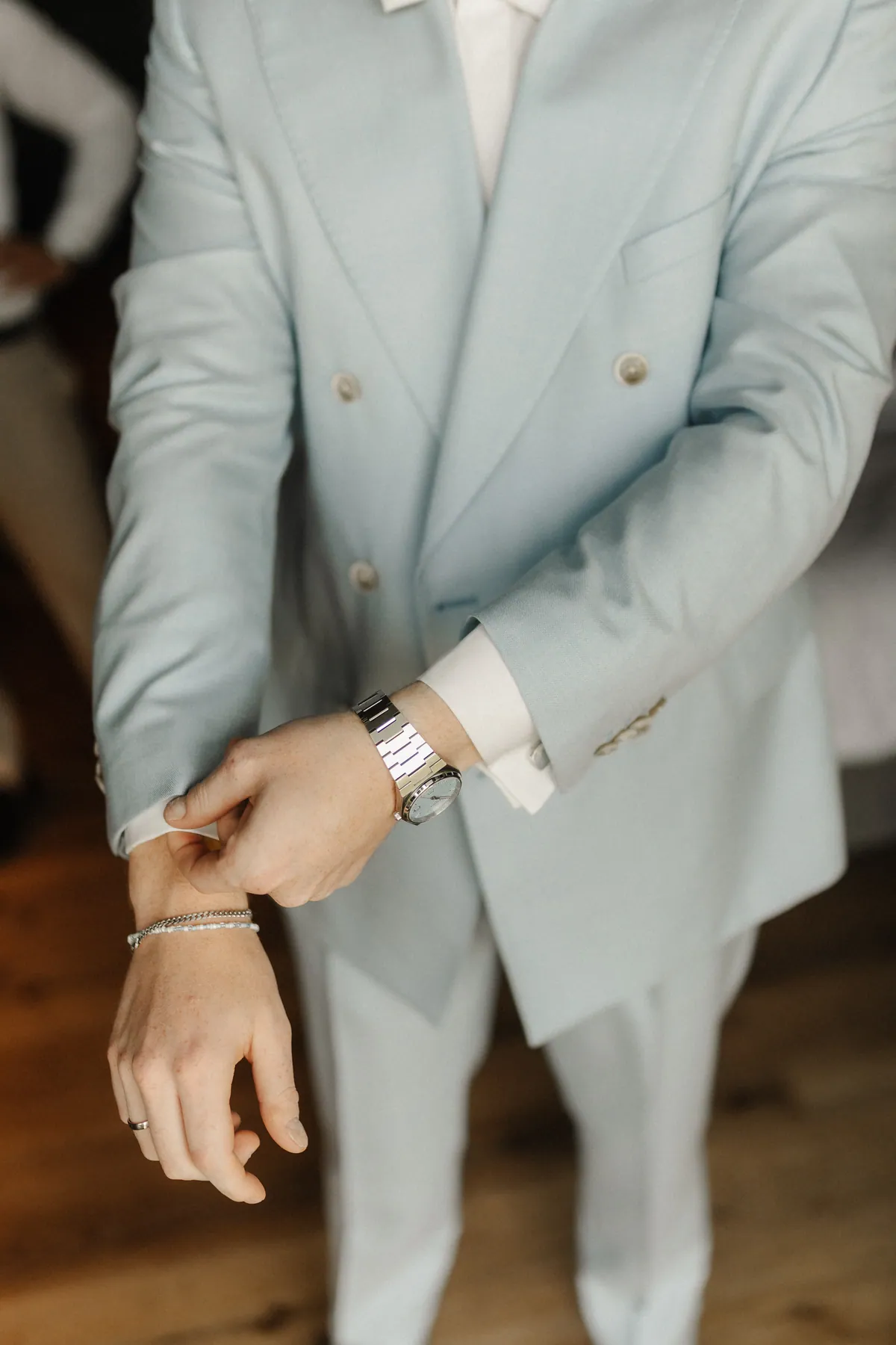 Leon zieht die weiße Hemdmanschette unter dem Ärmel seines hellblauen Zweireihers hervor, am Handgelenk eine Stahluhr mit hellblauem Zifferblatt, am Finger ein schmaler Ring.