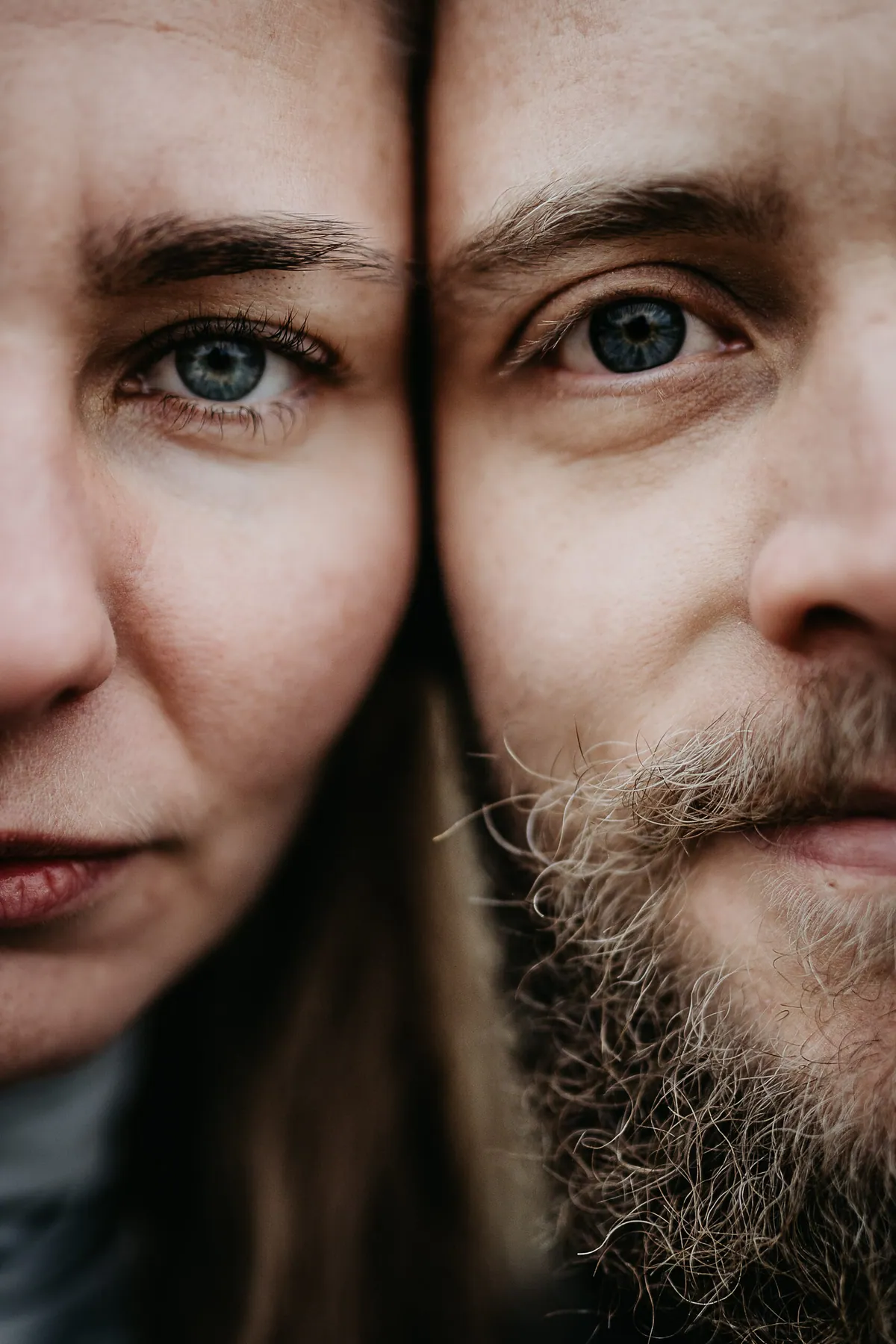 Extreme Nahaufnahme: Je eine Gesichtshälfte von ihr und ihm dicht aneinander, beide schauen mit blauen Augen direkt in die Kamera, rechts sein Bart.