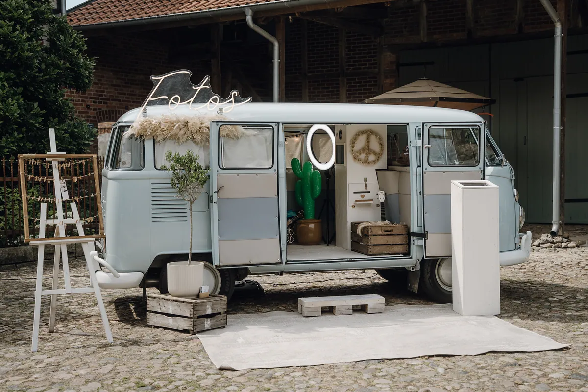 Ein hellblauer VW-Bus als Fotobox mit Leuchtschrift «Fotos», Pampasgras, Ringlicht und Kaktus, davor ein Teppich auf dem Kopfsteinpflaster und eine Staffelei.