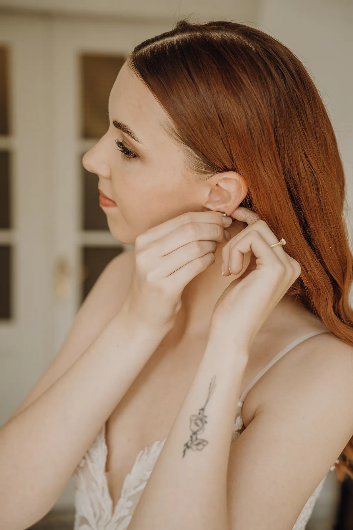 Im Profil steckt sich Theresa einen Ohrring an, das rote Haar fällt über die Schulter, am Unterarm ein feines Blumentattoo, am Finger ein Ring mit Stein.